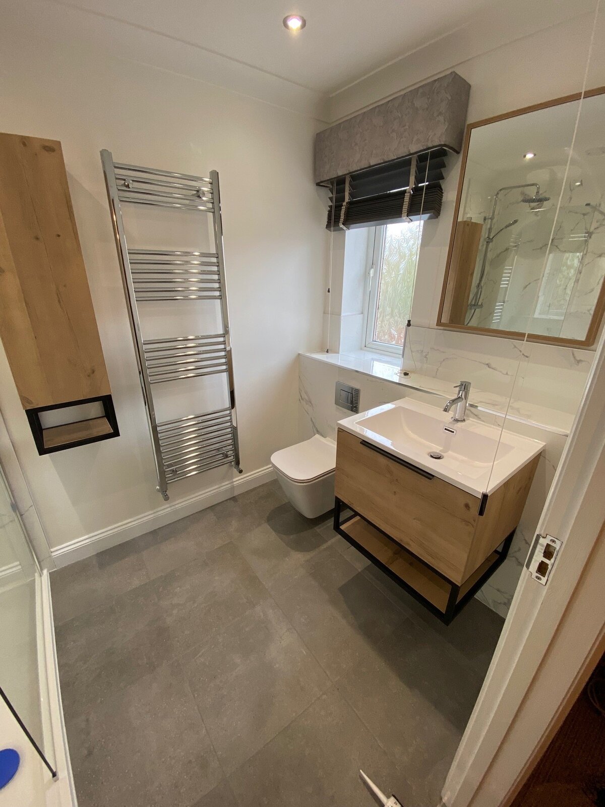 Bathroom with oak vanity, chrome towel rail and marble tiles