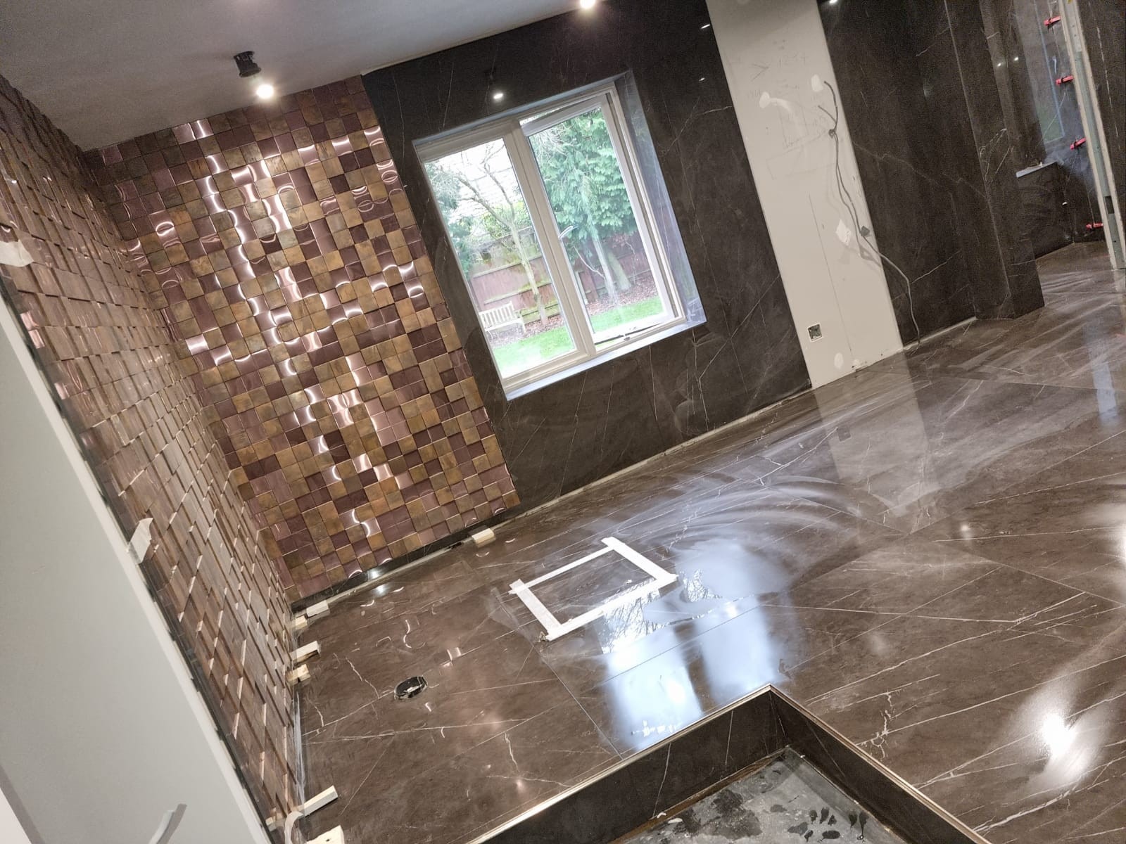 Large feature bathroom in progress with full marble effect tiles and copper mosaic feature wall