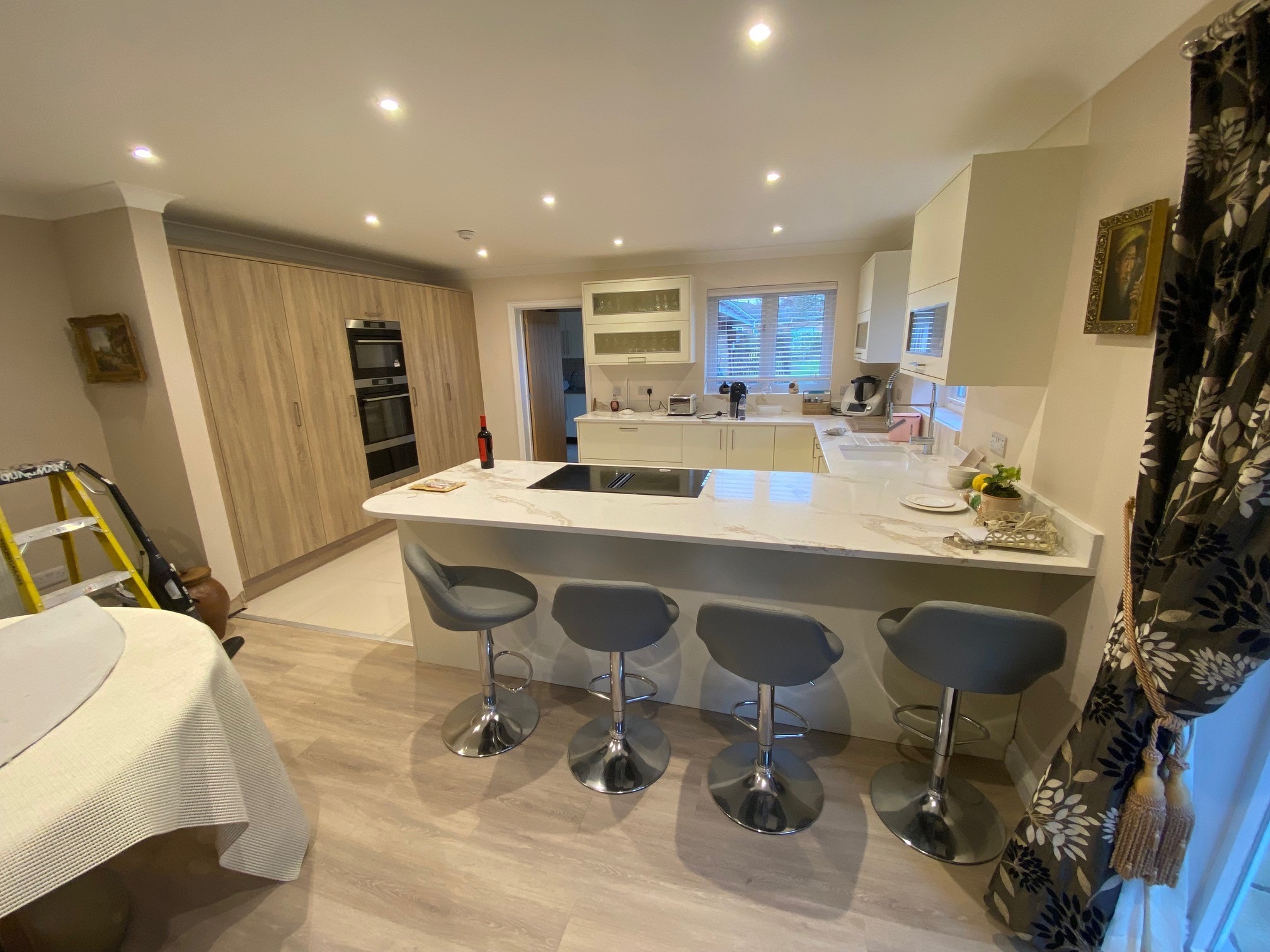 Open plan kitchen with large quartz waterfall peninsula, oak tower units and bar stools